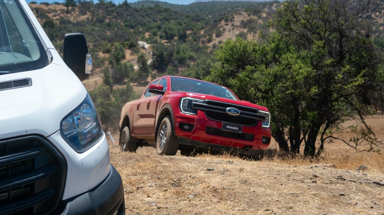Ford Ranger roja en un sendero de tierra con una Ford Transit blanca en primer plano, mostrando vehículos en un entorno off-road.